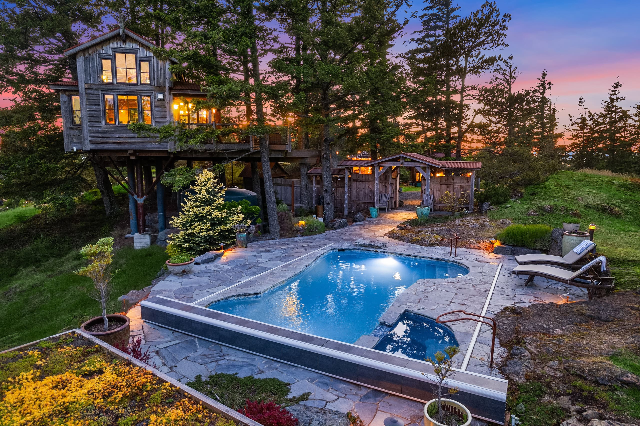 Charming outdoor space featuring a rustic treehouse and a serene pool area, surrounded by lush greenery, set against a vibrant twilight sky in the Pacific Northwest.