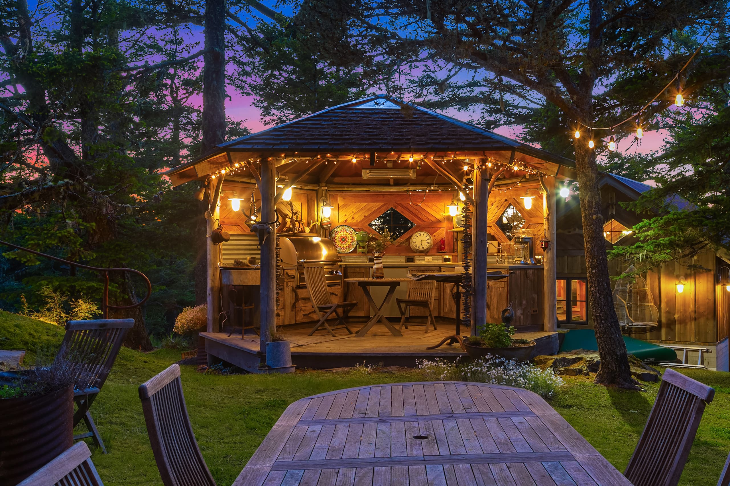 Charming outdoor kitchen with rustic wooden design, illuminated by string lights, set against a twilight backdrop in the Pacific Northwest.
