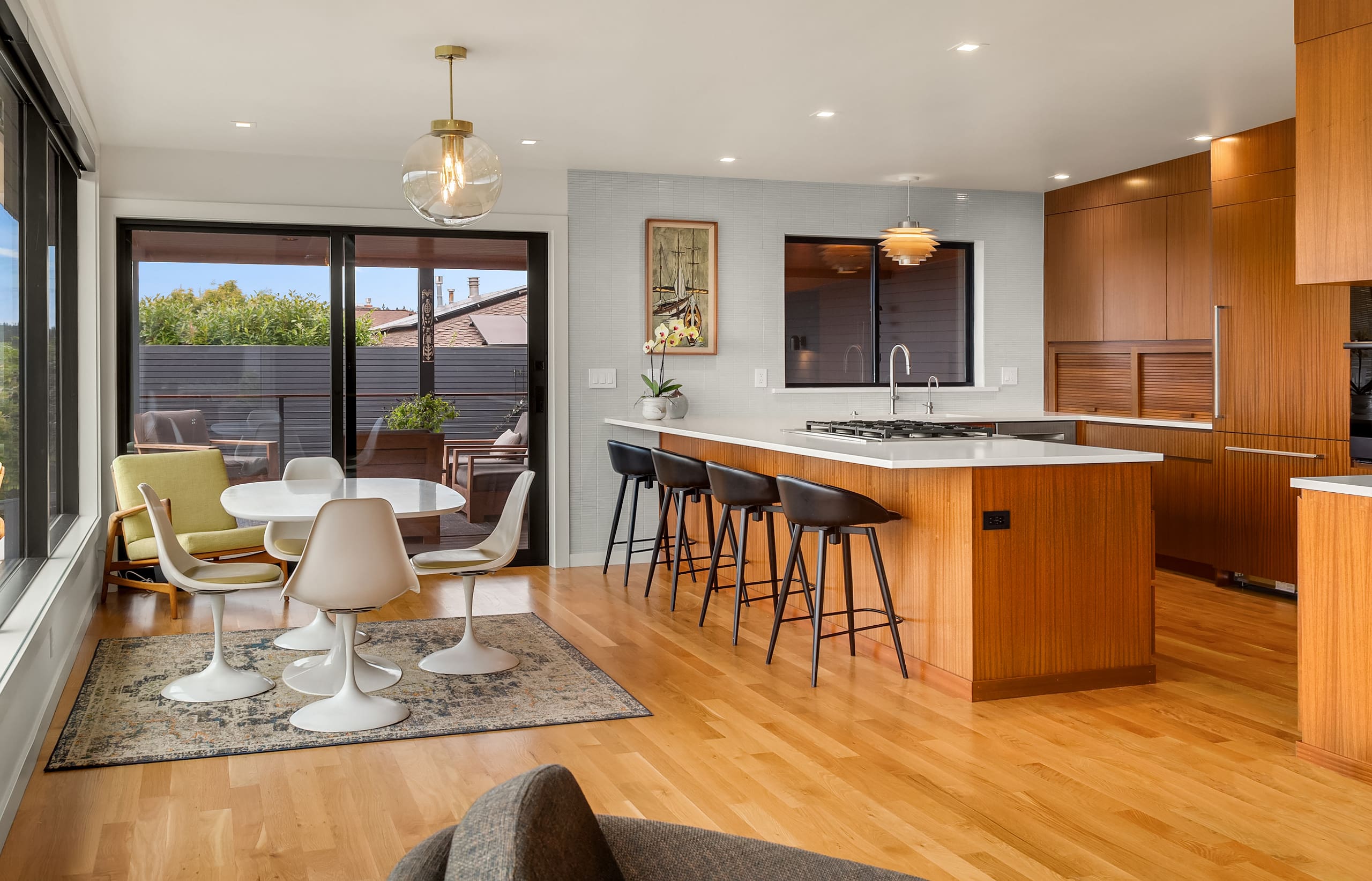 Modern kitchen and dining area featuring sleek wood cabinetry, a large island, and stylish seating, with abundant natural light and a view of outdoor greenery, located in the Pacific Northwest.