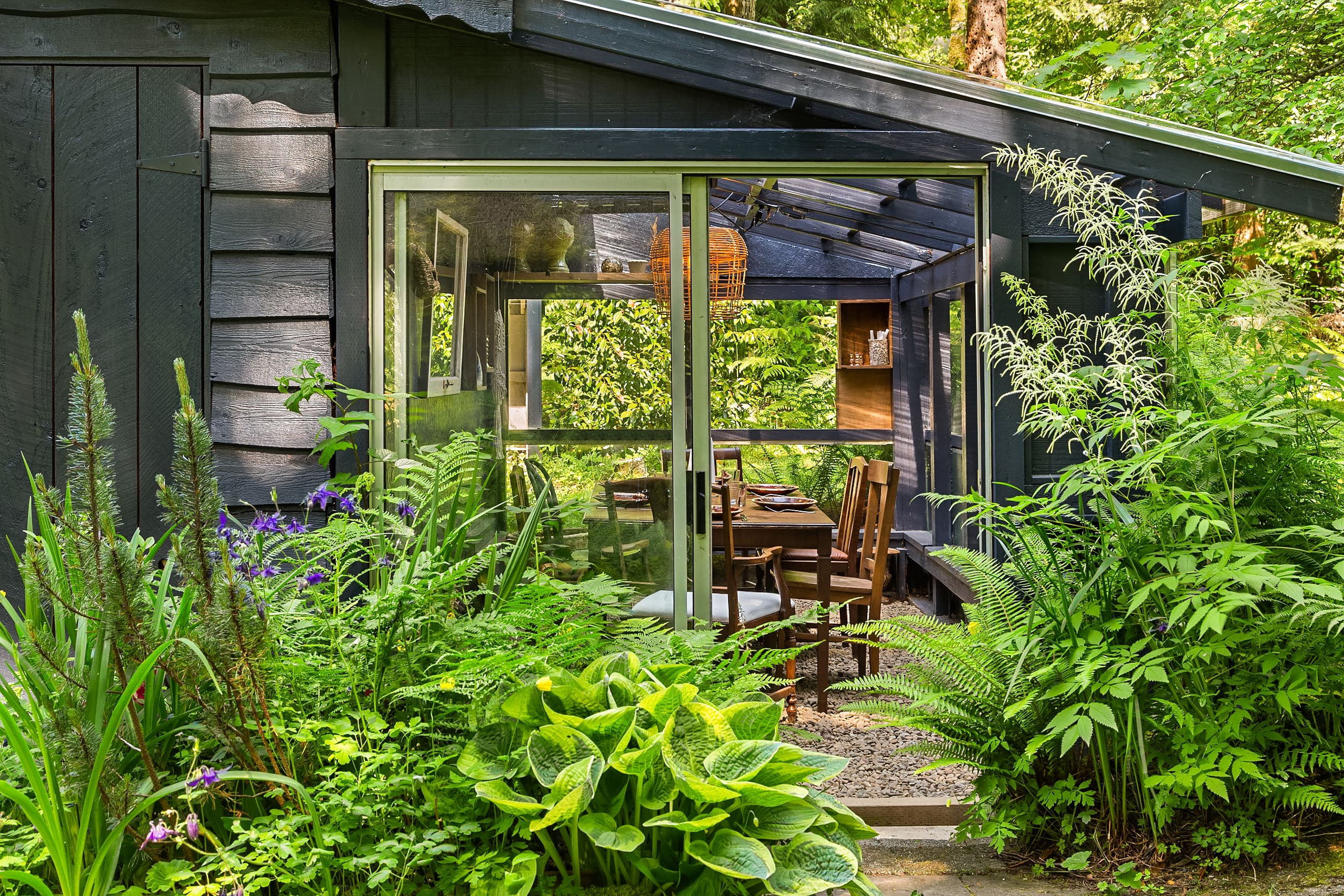 Charming outdoor dining area surrounded by lush greenery, featuring a modern design with large glass doors and a rustic wooden table, located in the Pacific Northwest.