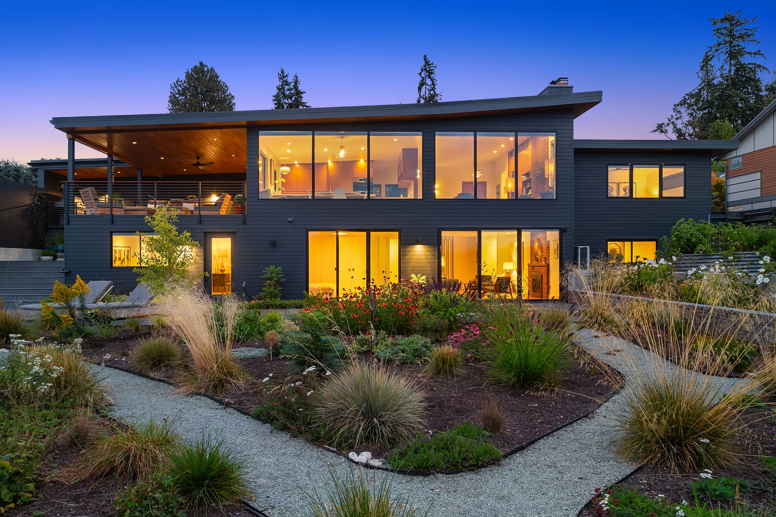 Modern exterior of a stylish home in Seattle, featuring large windows that illuminate the interior, surrounded by a beautifully landscaped garden at twilight.