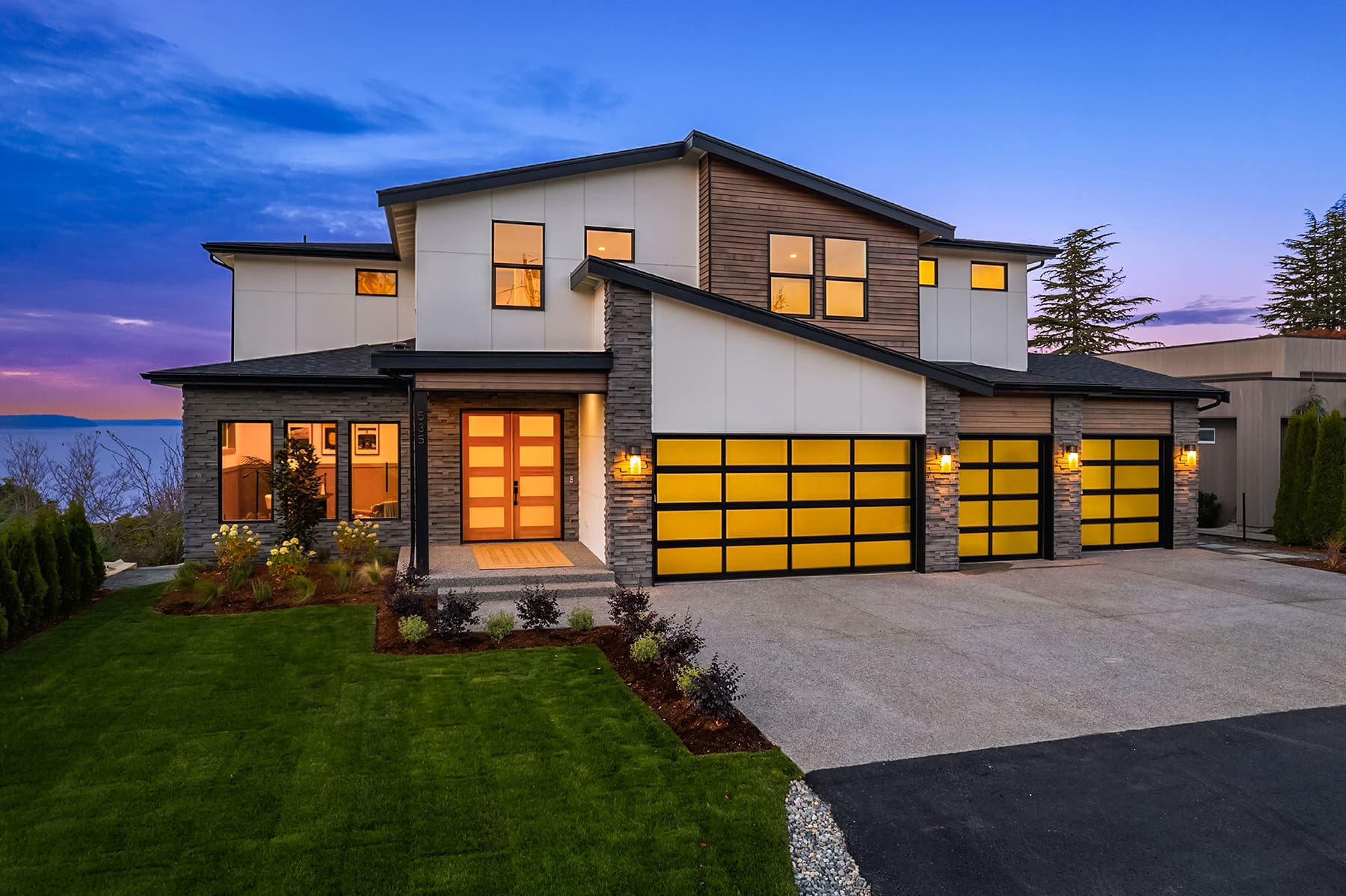 Modern exterior of a contemporary home featuring sleek lines, stone accents, and large yellow garage doors, set against a twilight sky in the Pacific Northwest.