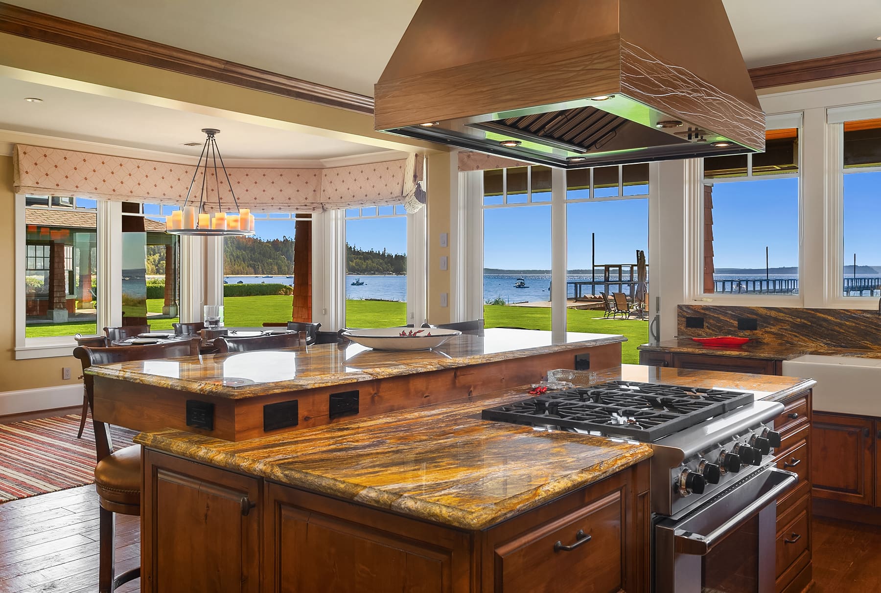 Spacious waterfront kitchen with modern design, featuring a large granite island, stainless steel appliances, and panoramic views of the lake and greenery, located in the Pacific Northwest.