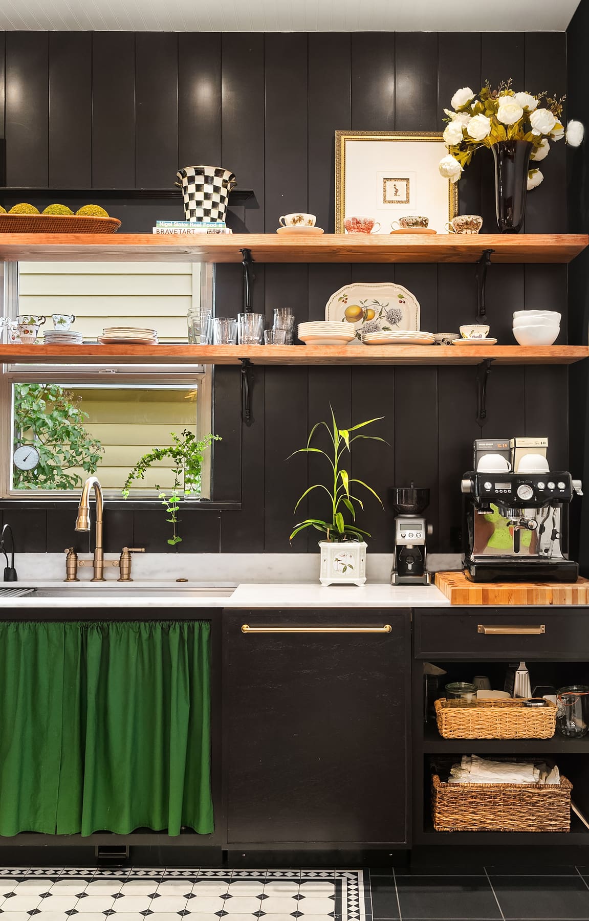 Modern kitchen featuring black shiplap walls, open wooden shelving, and a striking green curtain under the sink. Elegant design elements include brass fixtures and a coffee station, set in a charming Pacific Northwest home.