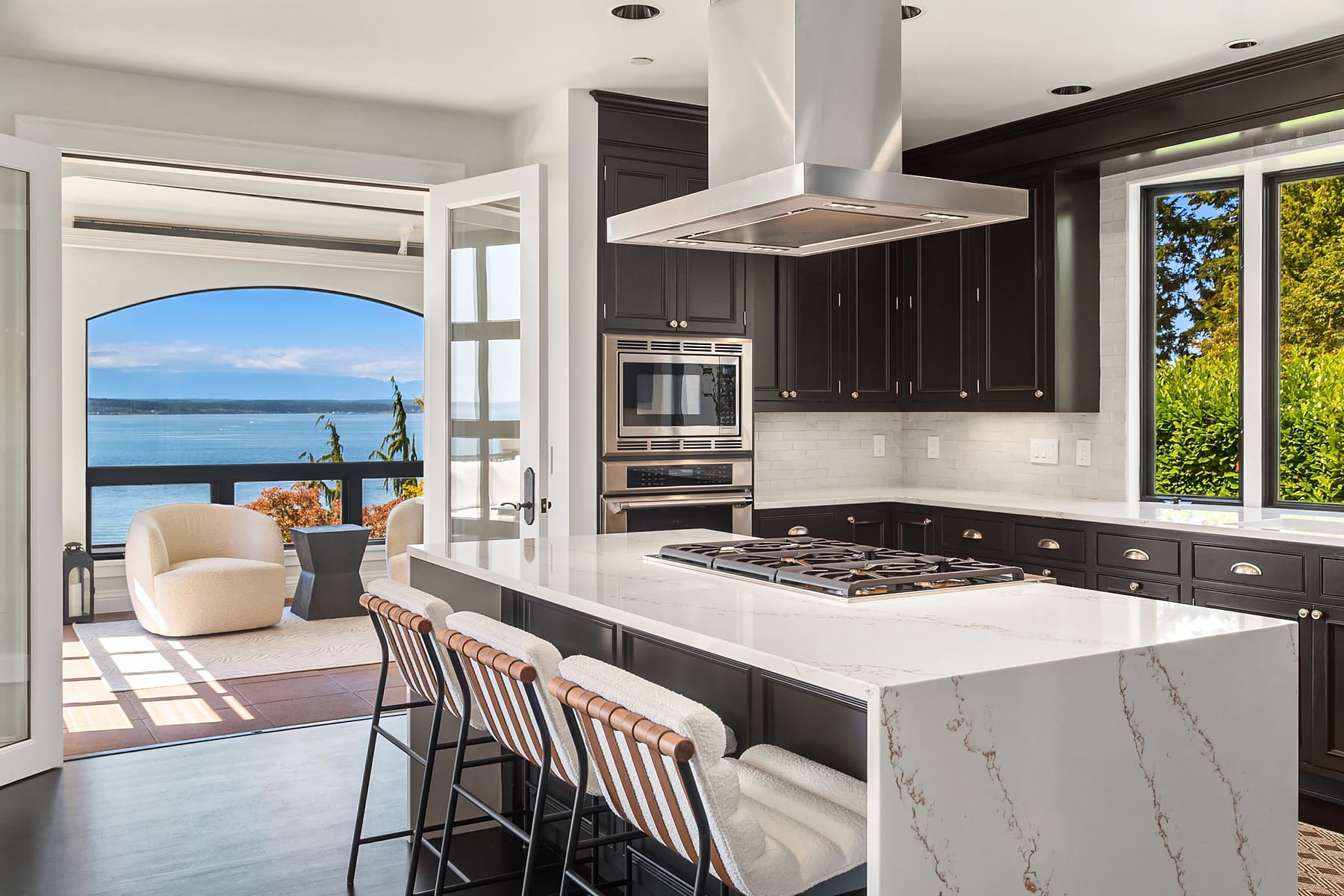 Modern kitchen with sleek black cabinetry, white marble countertops, and a stunning water view, located in the Pacific Northwest.