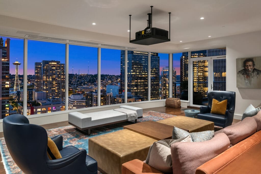 Modern living room with panoramic city views at twilight, featuring stylish seating, a projector, and elegant decor, located in Seattle.