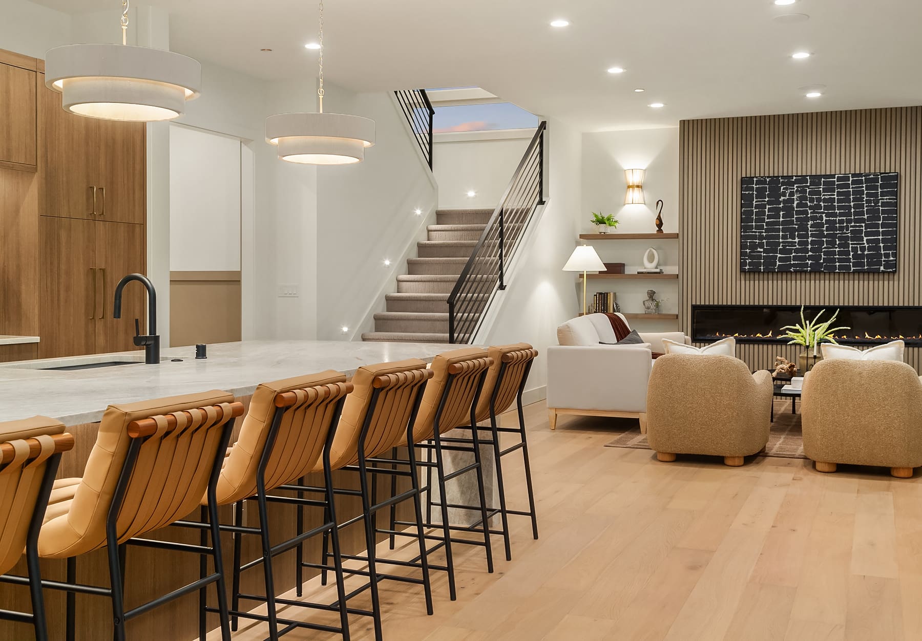 Modern open-concept living space featuring a stylish kitchen with a large marble island and sleek bar stools, leading to a cozy seating area with a contemporary fireplace. Located in the Pacific Northwest, this design combines elegance with warmth, ideal for both entertaining and relaxation.