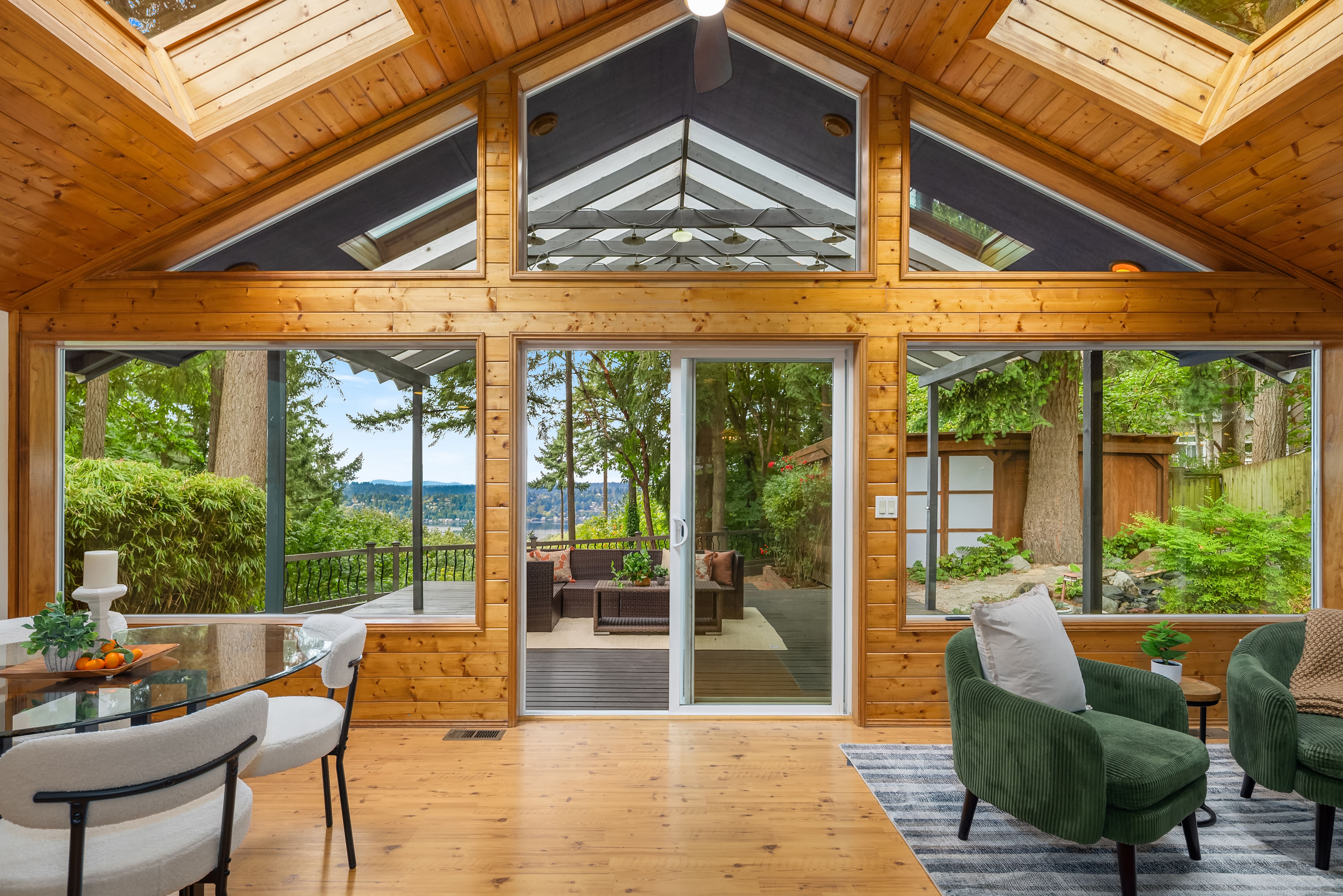 Cozy modern living room with vaulted wooden ceilings and large windows showcasing a scenic view, featuring stylish green chairs and a dining table, located in the Pacific Northwest.